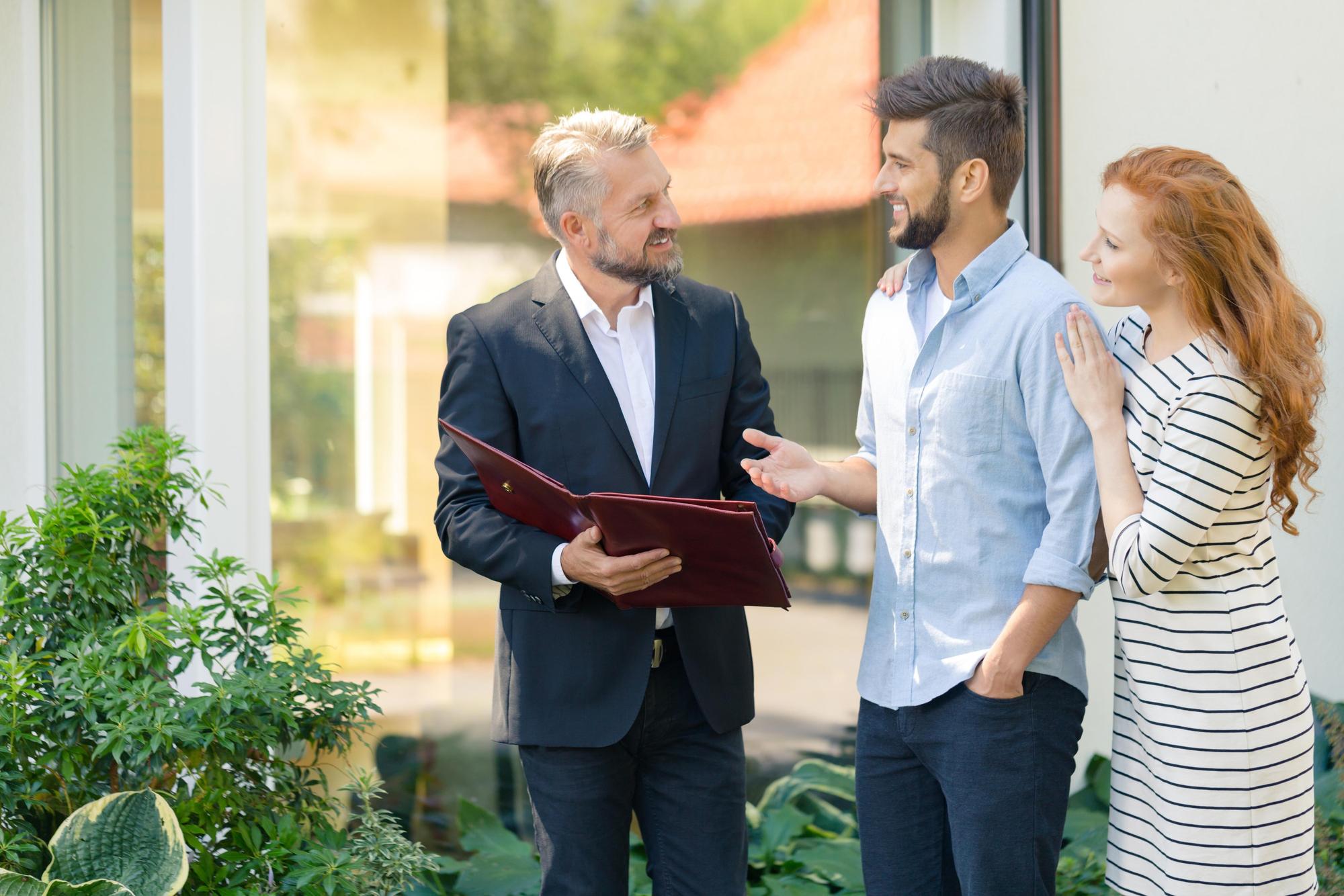 Agent imobiliar discutând cu proprietarul lângă o casă